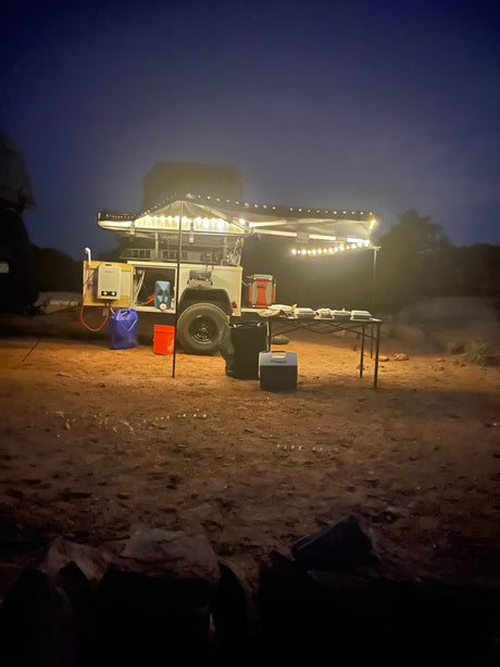 Nighttime off-grid desert camping with an RV rental. An illuminated overland trailer setup provides a cozy, comfortable mobile camp experience.