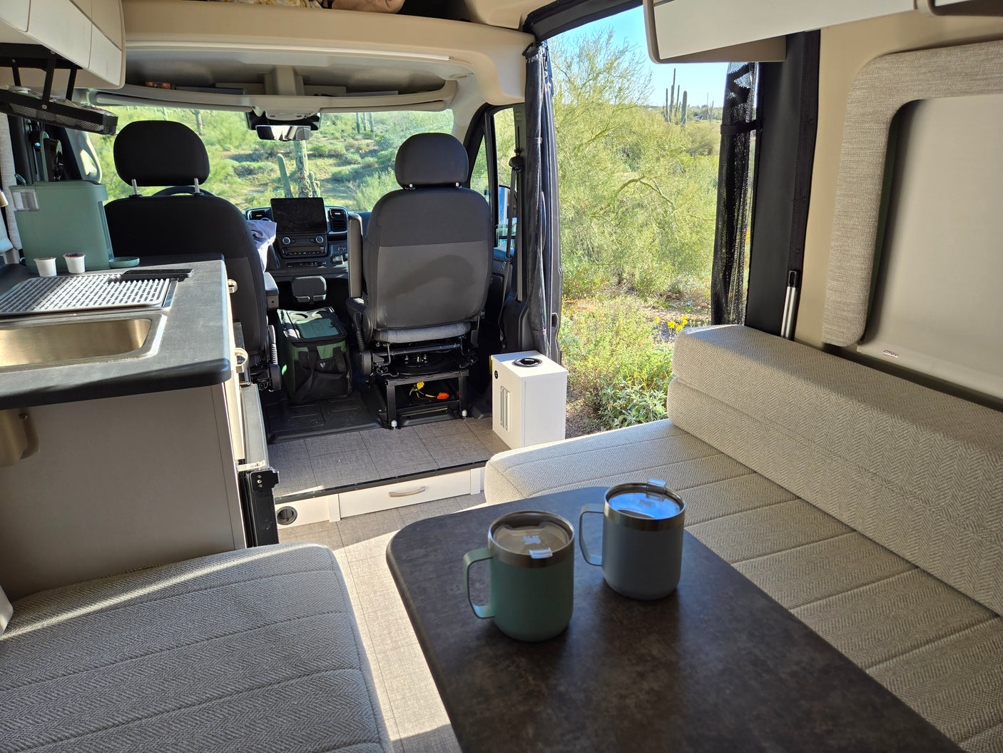 Cozy RV rental interior with desert views, coffee mugs on the table, and a functional kitchen. Perfect for adventure!