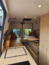 Inside a modern RV rental: bamboo cabinets, comfy mustard seating, a versatile table, and built-in amenities for travel.