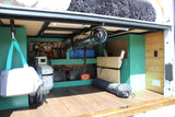 RV rental van's organized under-bed storage: propane, batteries, inverter, and electrical system visible on a wooden floor.