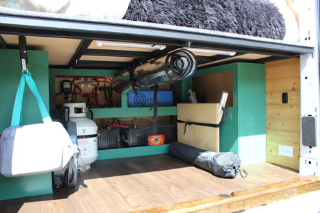 RV rental van's organized under-bed storage: propane, batteries, inverter, and electrical system visible on a wooden floor.
