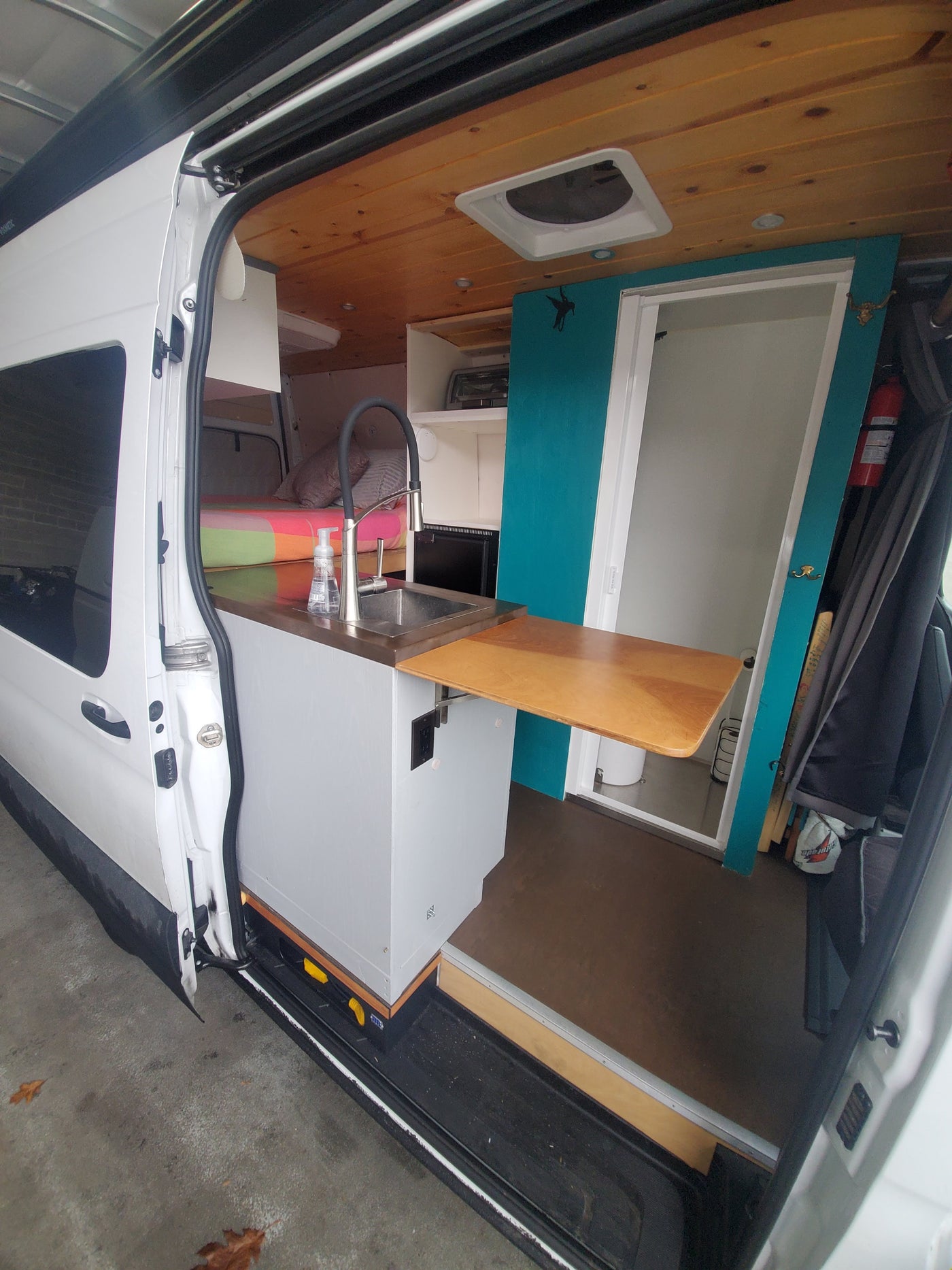 This RV rental interior boasts a modern kitchen with sink, cozy bed, and private shower/toilet area, ready for adventure. — photo 9