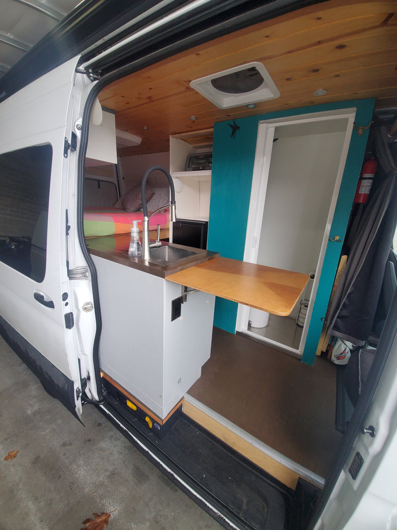 This RV rental interior boasts a modern kitchen with sink, cozy bed, and private shower/toilet area, ready for adventure. — photo 9