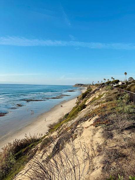 Coastal beach view from bluffs, ocean and people below. An RV is parked by cliffside homes, perfect for an RV rental vacation.