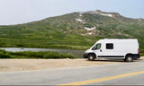White camper van RV rental parked by a scenic mountain lake. Perfect for adventure travel.