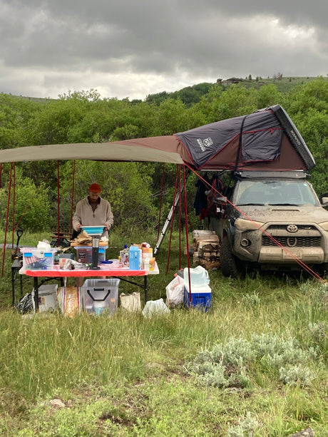 Camping kitchen setup with an overland vehicle, rooftop tent, and awning. Experience the outdoors like an RV rental adventure!