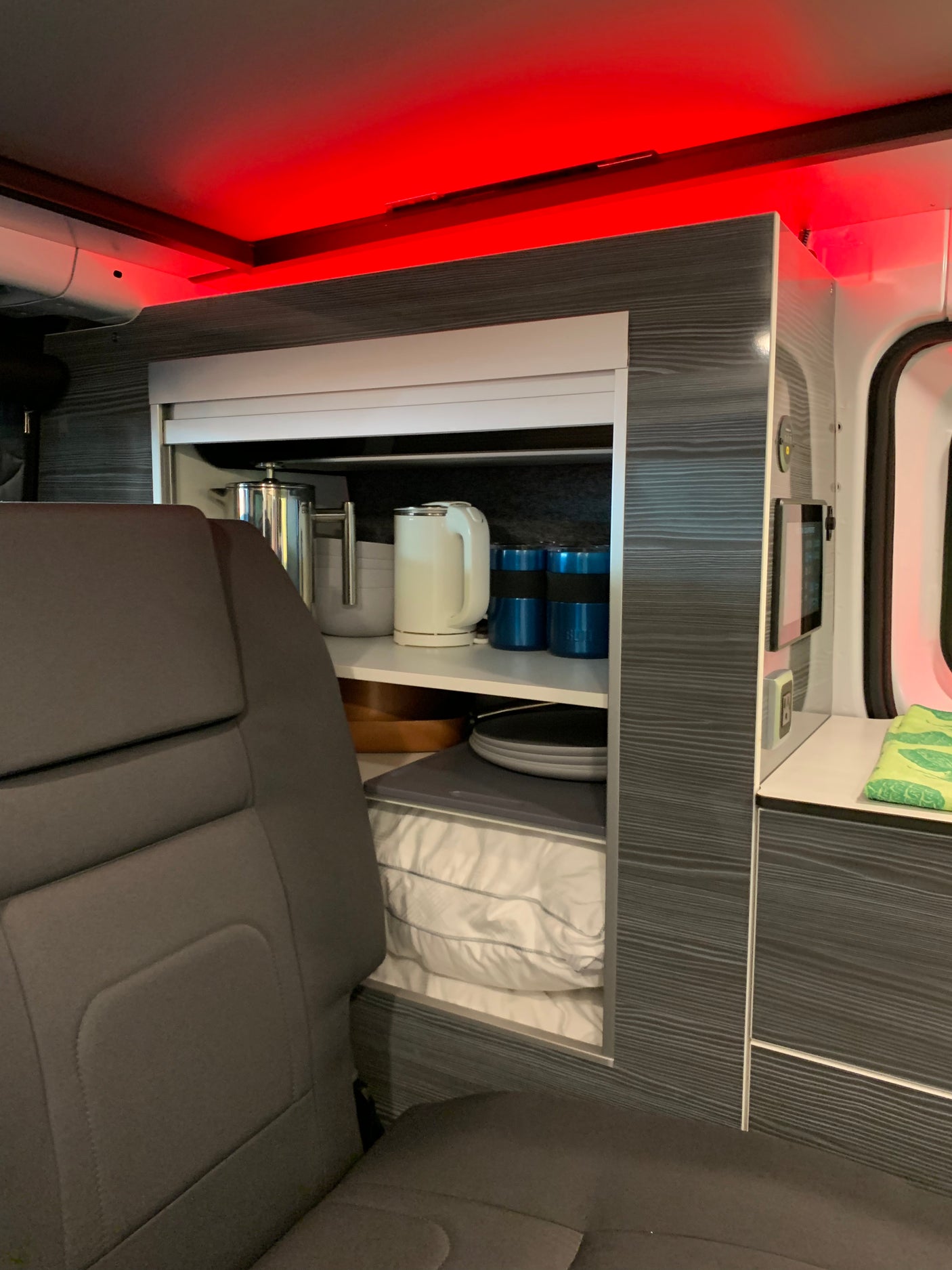Modern RV rental interior with red accent lighting, showing organized kitchen storage and cozy bedding.