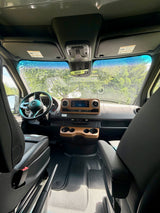 RV rental interior: modern driver's cockpit with Mercedes dashboard, navigation display, wood trim, and comfortable front seating.