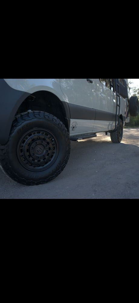 White rv rental camper van with rugged off-road tires, black wheels, side steps, and a rear ladder. Ideal adventure vehicle.