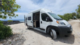 White RV rental camper van on a sandy, rocky beach. Ocean and volcanic shoreline in background. Perfect for nature adventures.