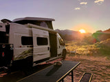 A white RV rental camper van with its pop-top extended at sunrise, parked with a stunning mountain view.