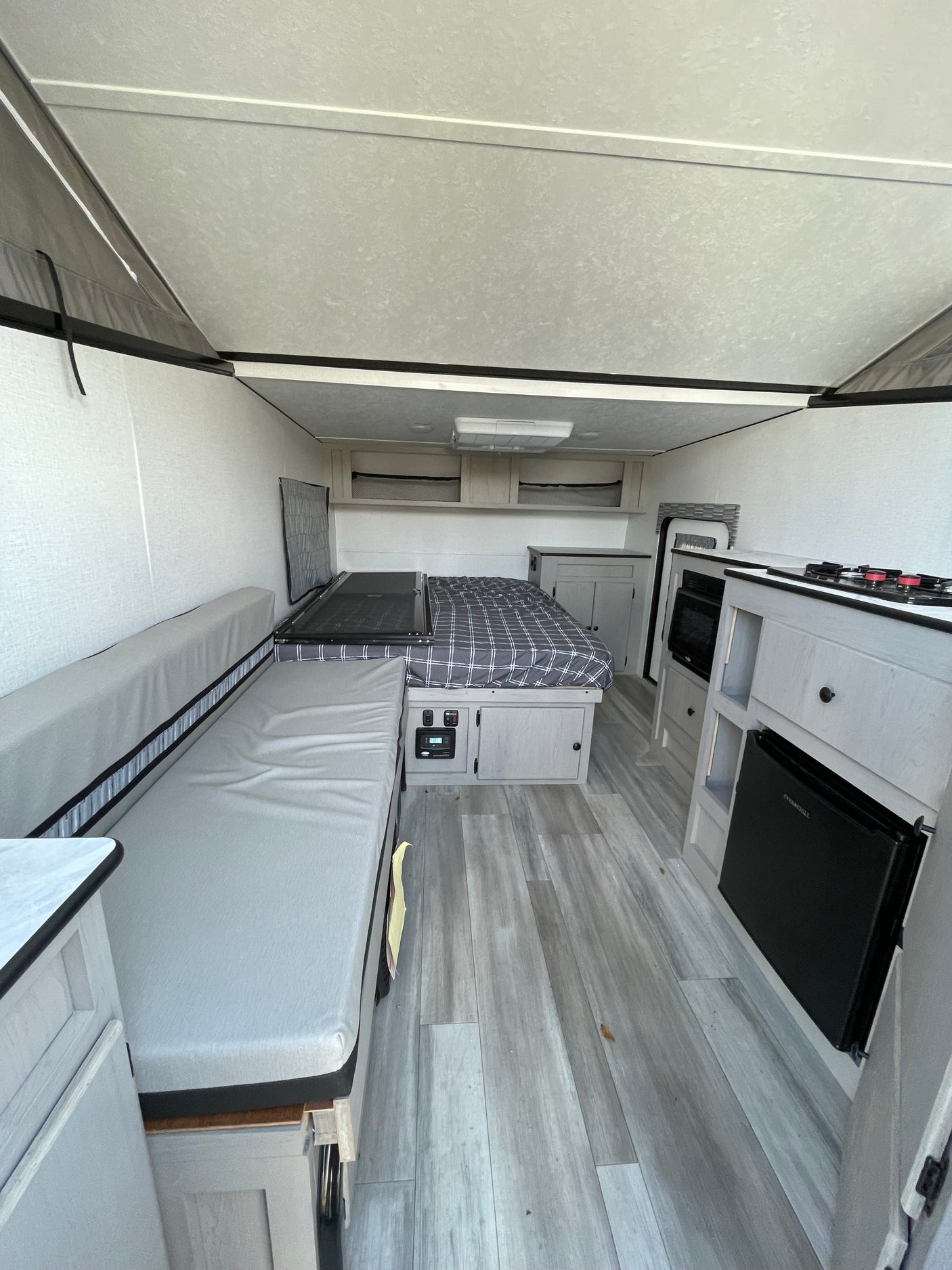 Experience comfort in this RV rental interior: cozy bed, long sofa, and a compact kitchen with stove, microwave, and mini-fridge.