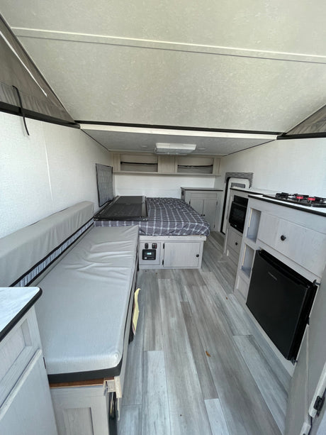 Experience comfort in this RV rental interior: cozy bed, long sofa, and a compact kitchen with stove, microwave, and mini-fridge.