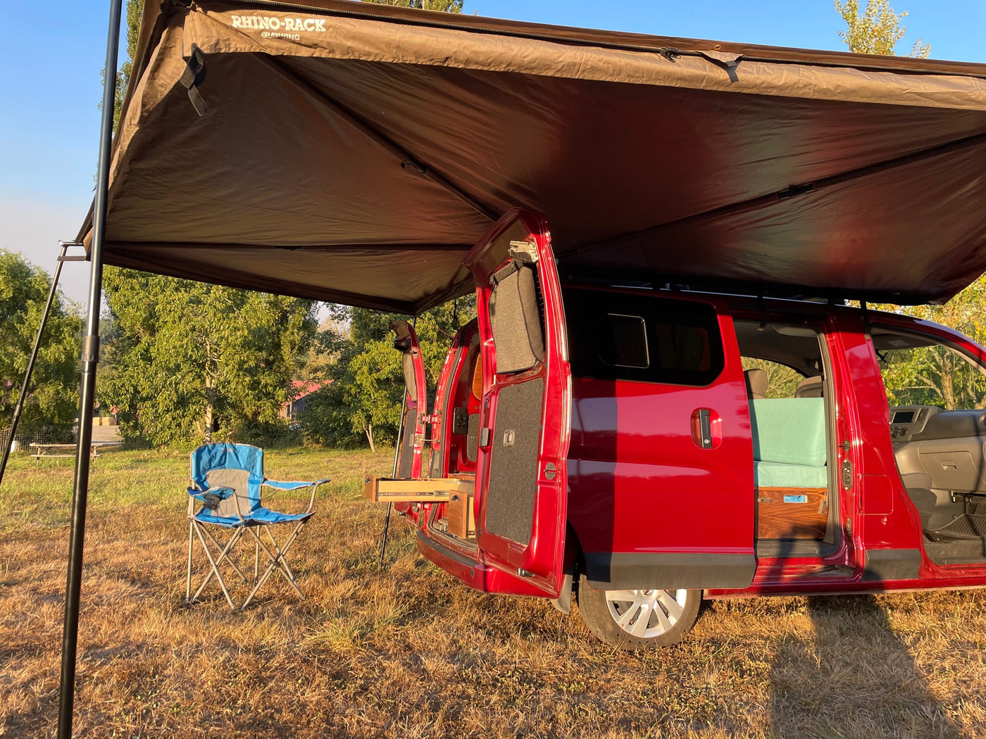 A red camper van RV rental with an open side, revealing a custom interior, parked under an awning with a chair outside. — photo 7