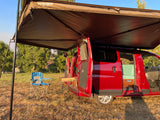 A red camper van RV rental with an open side, revealing a custom interior, parked under an awning with a chair outside.