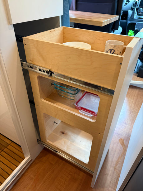Organized RV rental kitchen with a wooden pull-out pantry, holding dishes and glass food containers.