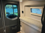 An RV rental's inviting interior: rear door window shows a mounted tire, a comfy bench, and a side window with blinds.
