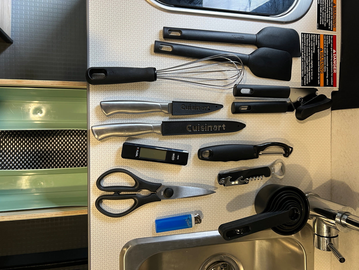 An RV rental kitchen counter organized with essential cooking tools: spatulas, whisk, knives, measuring cups, and a digital thermometer.