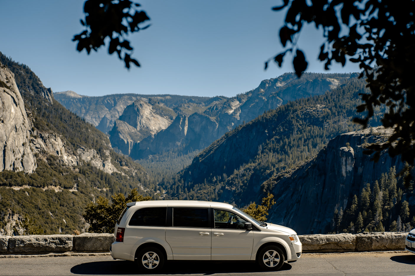 A white minivan, an alternative to an RV rental, at a scenic Yosemite overlook. Majestic mountains fill the background.