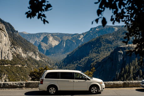 White minivan parked on a scenic road in Yosemite. Enjoy mountain views perfect for your next RV rental road trip.
