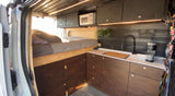 Compact rv rental interior with bed, kitchen, & microwave. Ideal for mobile living.
