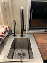 RV rental kitchen: stainless steel sink, dual black faucets, and a cozy textured blanket, ready for adventures.