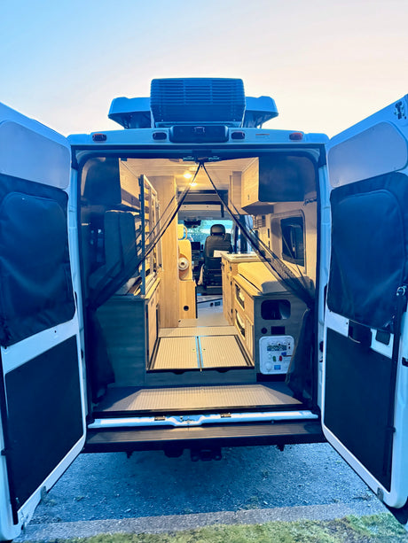 Open rear doors of an RV rental reveal its custom campervan interior, featuring cozy built-in living and sleeping areas.