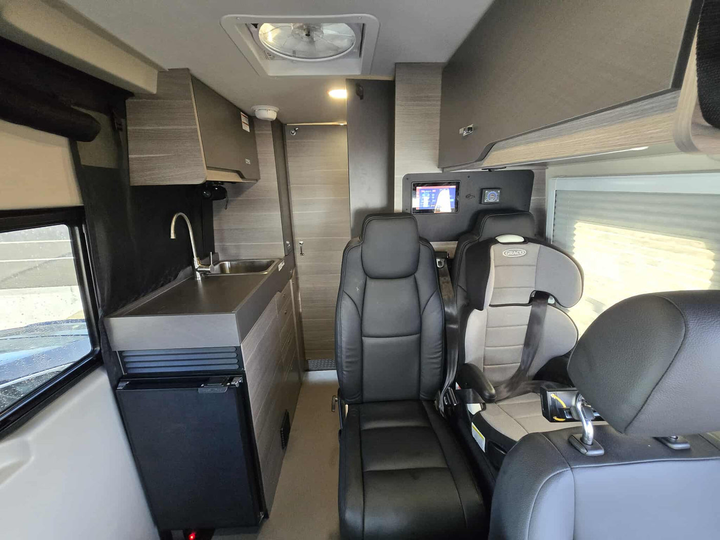 RV rental interior showcasing a compact kitchen, seating, and a child car seat, perfect for family road trips.