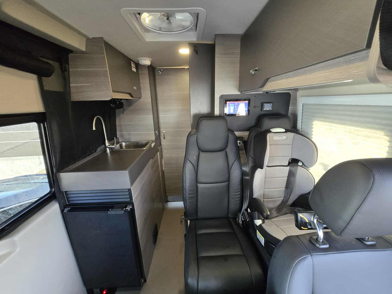  fireside next to a parked camper van with an awning extended by the road.|RV rental: Compact camper van interior with a kitchen counter — photo 11