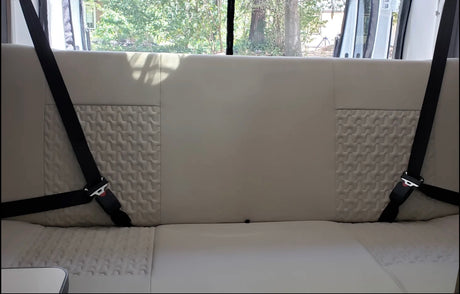 An RV rental's rear interior features a light bench seat, textured back panels, and two visible safety seatbelts.