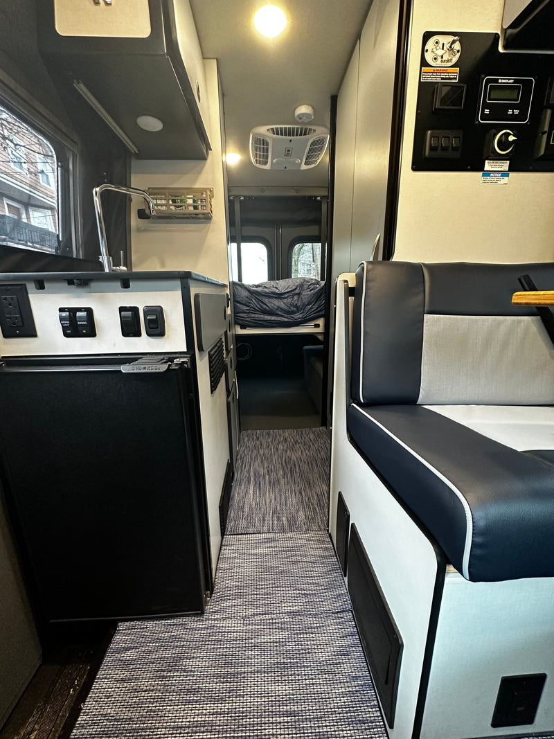 Step inside this RV rental's compact interior, featuring a kitchen with a sink, comfortable seating, and a bed in the rear. — photo 14