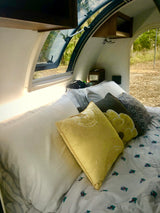 Enjoy a cozy night's sleep in this RV rental! Interior view of a comfortable bed with colorful pillows and an open window.
