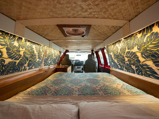 Inside this RV rental: a cozy bed with patterned quilt, tropical leaf wall decor, and a woven bamboo ceiling.