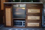 Inside an RV rental: a modern galley with custom walnut & maple burl cabinetry, stainless fridge, microwave, and power panel.