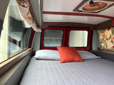 Enjoy this RV rental's comfy interior: a bed with white/orange pillows, custom wood accents, and back windows.
