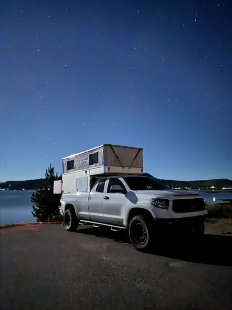 Stargazing from an RV rental: a white truck with a pop-up camper by a lake at night. Perfect for outdoor adventure & camping.