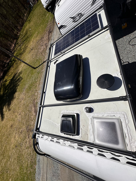 Top-down view of an RV rental roof featuring solar panels, a Dometic AC unit, vents, and a roof access rack.