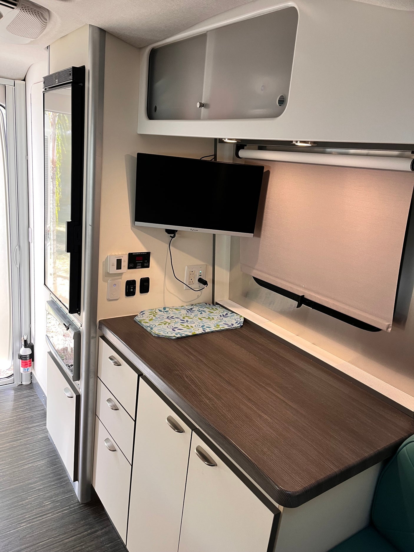 RV rental interior: compact kitchen counter, fridge, mounted TV, control panel, and overhead storage.