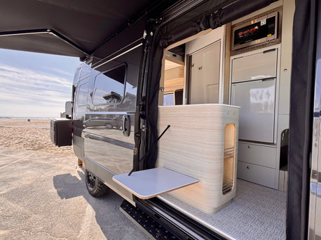 Explore this RV rental's mobile kitchen with microwave, fridge, and fold-out table, under an extended awning at the beach.