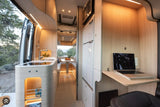Spacious RV rental interior featuring a modern kitchen, dining area, overhead bed, and a laptop on a dedicated workspace.