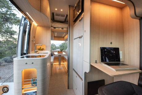 Spacious RV rental interior featuring a modern kitchen, dining area, overhead bed, and a laptop on a dedicated workspace.