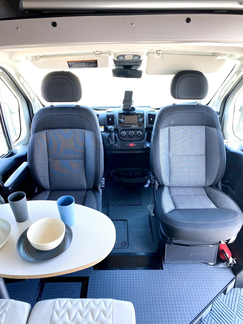 RV rental camper van interior: front cabin with dual seats, dashboard, and dining table set for meals. — photo 10