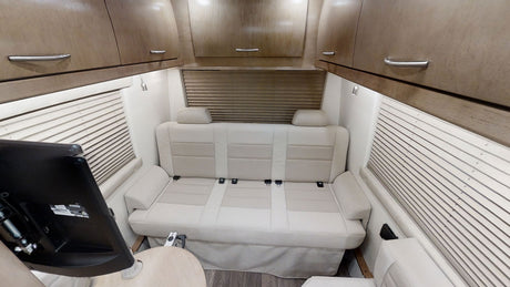 Inside an RV rental: a cream sofa converts to a bed, flanked by blinds & overhead cabinets, with a TV in view.