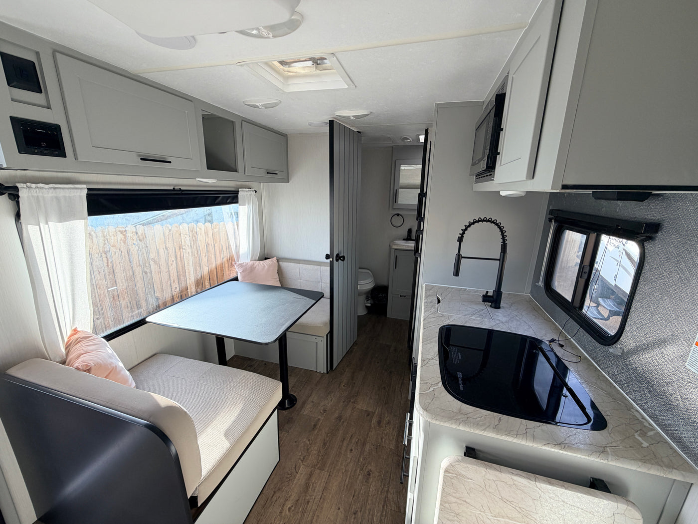Bright rv rental interior: dinette with table, modern kitchenette with sink, microwave, and light gray cabinets. — photo 3