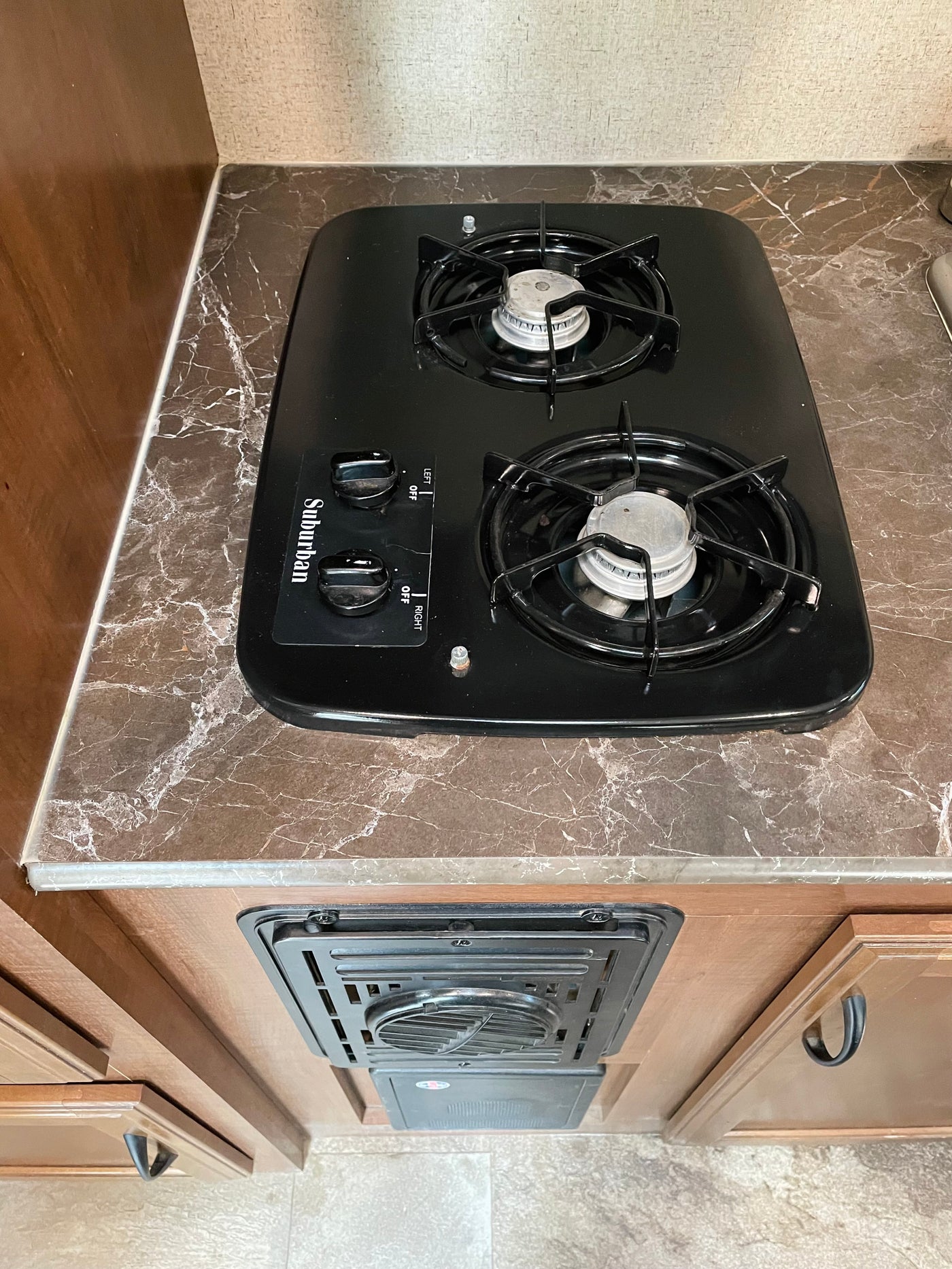View of an RV rental kitchen with a black Suburban two-burner stove on a marbled countertop, and a heating/cooling vent below. — photo 8