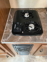 View of an RV rental kitchen with a black Suburban two-burner stove on a marbled countertop, and a heating/cooling vent below.