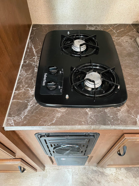 View of an RV rental kitchen with a black Suburban two-burner stove on a marbled countertop, and a heating/cooling vent below.