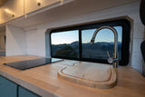 Compact RV kitchen with mountain views, featuring a wood counter, sleek cooktop, and modern faucet. Perfect for your RV rental adventure.
