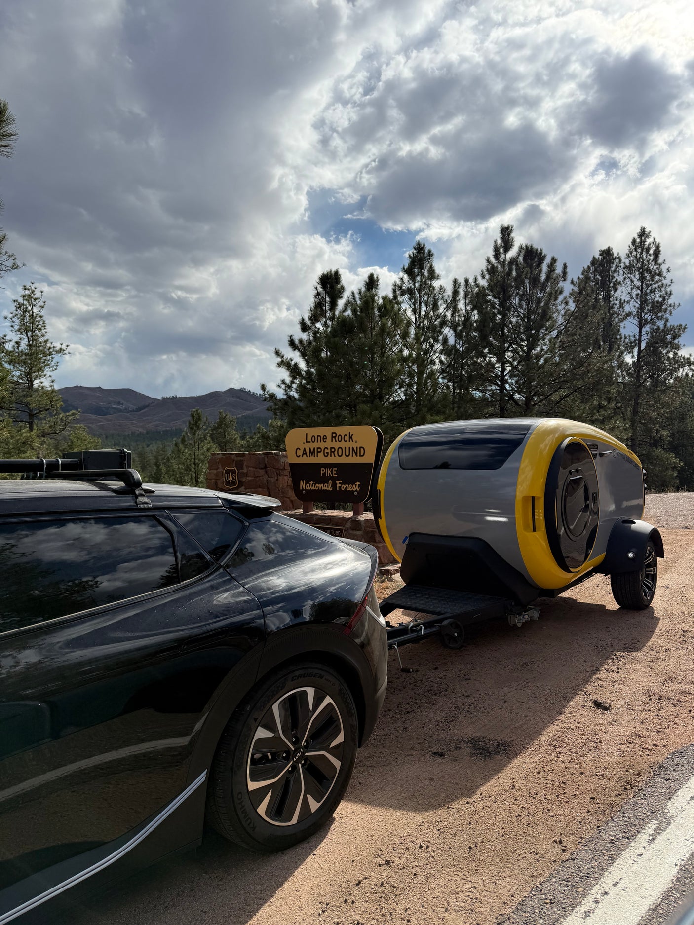 Modern Cortes RV rental for adventure at Lone Rock Campground, Pike National Forest, towed by a black car.