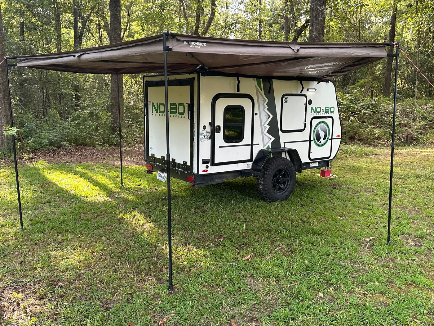 Explore nature! This small white camping trailer with an extended awning offers comfortable RV rental for outdoor travel in the woods. — photo 12